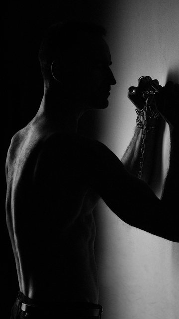 Silhouette von hinten, die Hand mit der Kette an der Wand.