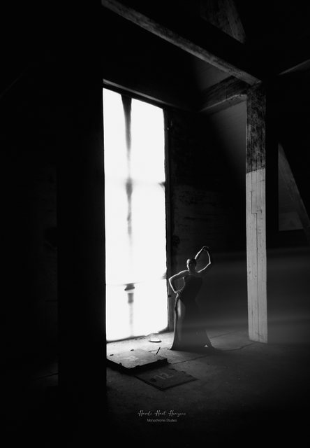 Sarah steht klein vor einem hohen, hellen Fenster im dunklen Speicherboden.
