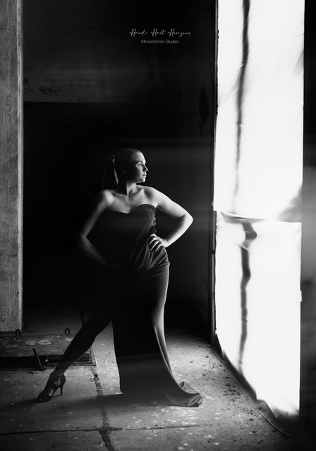 Sarah im langen Kleid am Fenster, eine Hand an der Hüfte, der Blick ins Licht.